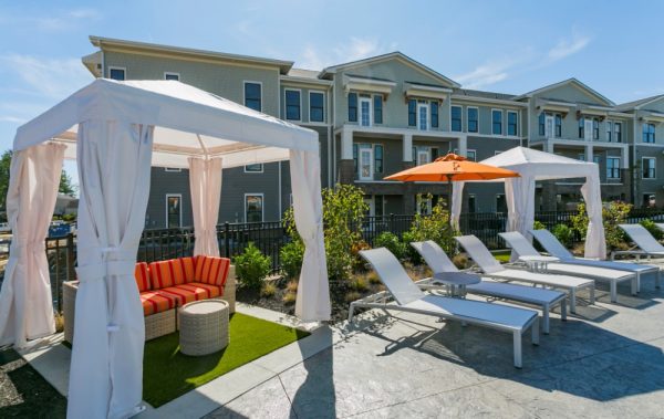Closeup of a poolside cabana with a couch on turf and lounge chairs nearby